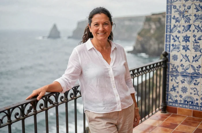 Femme souriante sur la terrasse d'une maison de pêcheur à Nazaré au Portugal avec vue sur l'océan Atlantique et carreaux azulejos